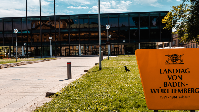 Der Landtag von Baden-Württemberg mit moderner Glasfassade und einem gelben Schild im Vordergrund. Im Hintergrund ist der Fernsehturm zu sehen., © Stuttgart-Marketing GmbH, Sarah Schmid Der Landtag von Baden-Württemberg mit moderner Glasfassade und einem gelben Schild im Vordergrund. Im Hintergrund ist der Fernsehturm zu sehen., © Stuttgart-Marketing GmbH, Sarah Schmid