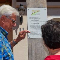 Zwei Personen lesen eine Gedenktafel an einem Holzpfosten. Die Tafel erinnert an historische Ereignisse in der Stadt Waldenbuch., © Natur.Nah. Schönbuch & Heckengäu