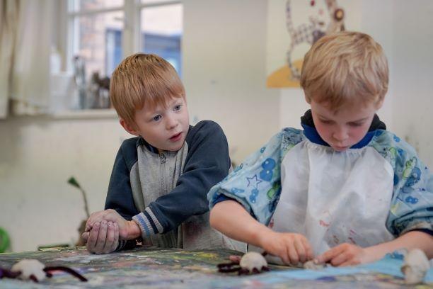 Zwei Jungen arbeiten konzentriert mit Ton an einem Tisch in einem kreativen Workshop. Einer trägt eine Schürze, der andere schaut interessiert zu., © Kunstschule Labyrinth Zwei Jungen arbeiten konzentriert mit Ton an einem Tisch in einem kreativen Workshop. Einer trägt eine Schürze, der andere schaut interessiert zu., © Kunstschule Labyrinth