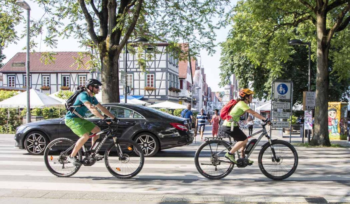 Zwei Radfahrer überqueren einen Zebrastreifen in einer Stadt mit Fachwerkhäusern. Im Hintergrund sind Fußgänger und Bäume zu sehen., © Schwäbische Alb Tourismusverband e.V.
