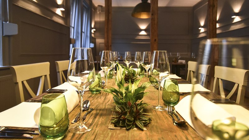 Ein stilvoll gedeckter Esstisch mit Weingläsern, grünen Gläsern und Pflanzen als Dekoration in einem eleganten Raum., © Classic Rock Café Gastronomie- Betriebs GmbH Ein stilvoll gedeckter Esstisch mit Weingläsern, grünen Gläsern und Pflanzen als Dekoration in einem eleganten Raum., © Classic Rock Café Gastronomie- Betriebs GmbH