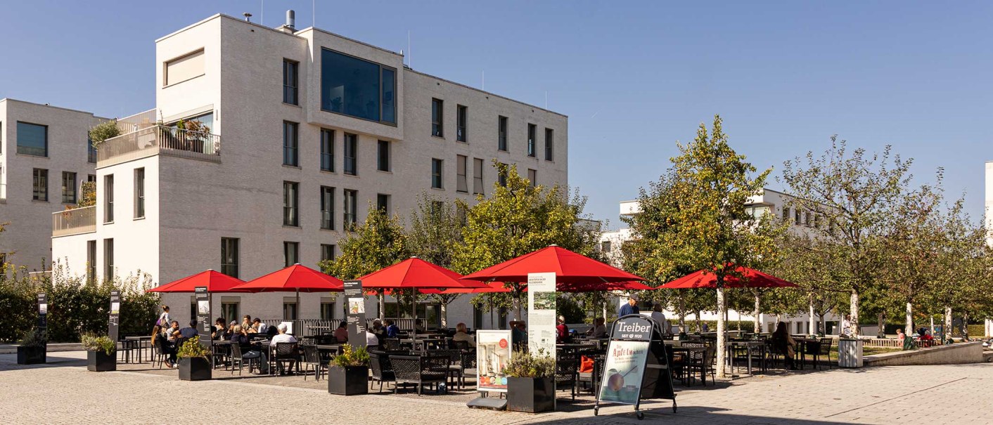 Moderne Wohngebäude in Stuttgart Killesberghöhe, mit roten Sonnenschirmen und Menschen auf einem Platz bei sonnigem Wetter., © Stuttgart-Marketing GmbH, Sarah Schmid