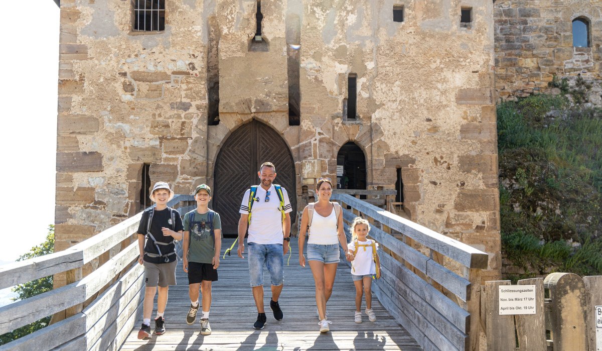 Eine Familie mit Rucksäcken geht über eine Holzbrücke zur Burgruine Hohenrechberg. Die Sonne scheint, und alle lächeln., © Foto Thomas Zehnder Eine Familie mit Rucksäcken geht über eine Holzbrücke zur Burgruine Hohenrechberg. Die Sonne scheint, und alle lächeln., © Foto Thomas Zehnder