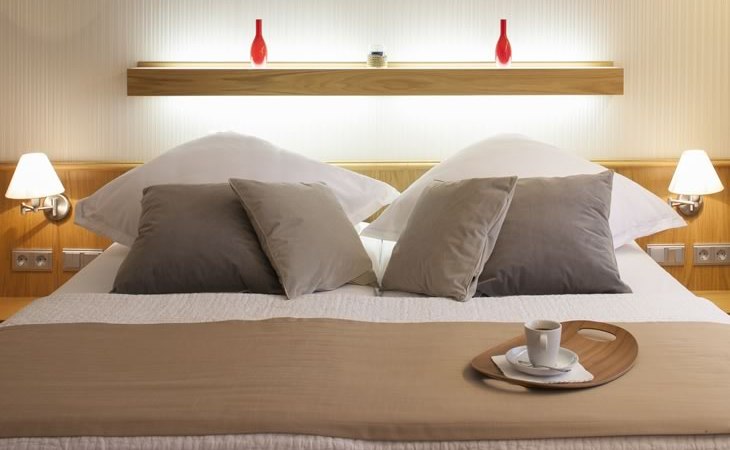Modernes Schlafzimmer mit Doppelbett, dekoriert mit Kissen und Tablett mit Tasse. Zwei rote Vasen auf einem Regal im Hintergrund., &copy; Hotel Drei Morgen