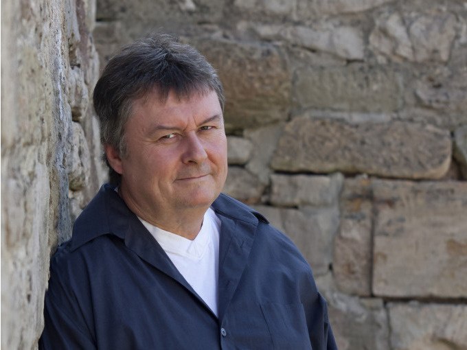 Ein Mann in dunkler Kleidung lehnt lächelnd an einer alten Steinmauer und blickt in die Kamera., © WTM GmbH Waiblingen