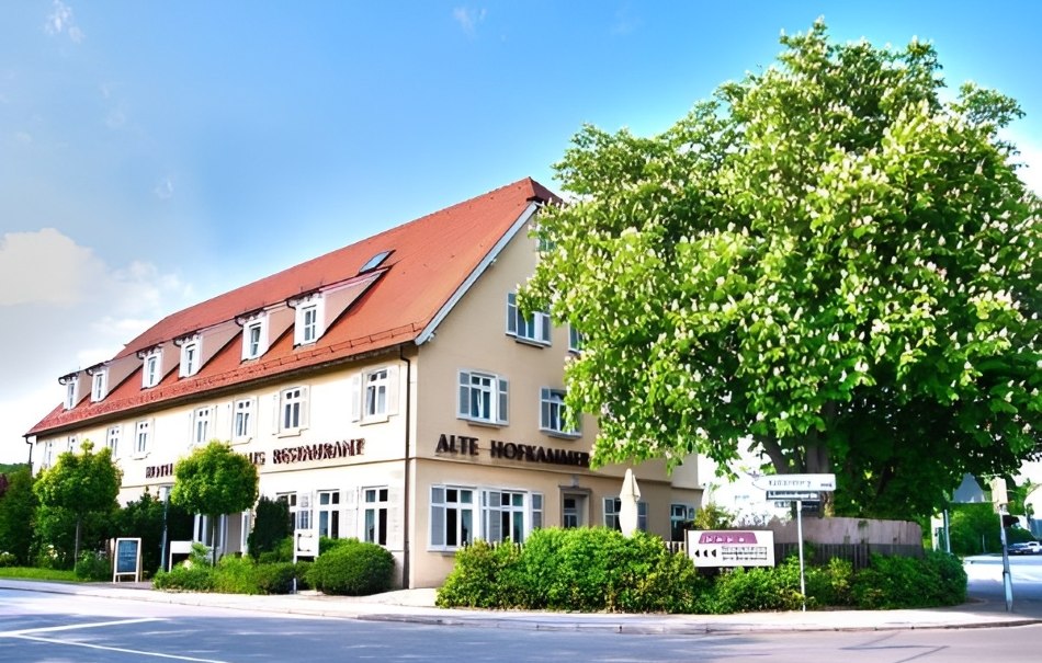 Ein Hotel mit rotem Dach und mehreren Fenstern, umgeben von Bäumen und Büschen, unter blauem Himmel., © Hotel Neuwirtshaus