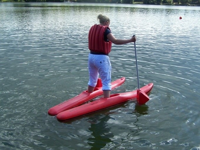Person mit Schwimmweste steht auf roten Wasserschuhen und paddelt auf einem See., © Cool-Tours StattReisen Person mit Schwimmweste steht auf roten Wasserschuhen und paddelt auf einem See., © Cool-Tours StattReisen