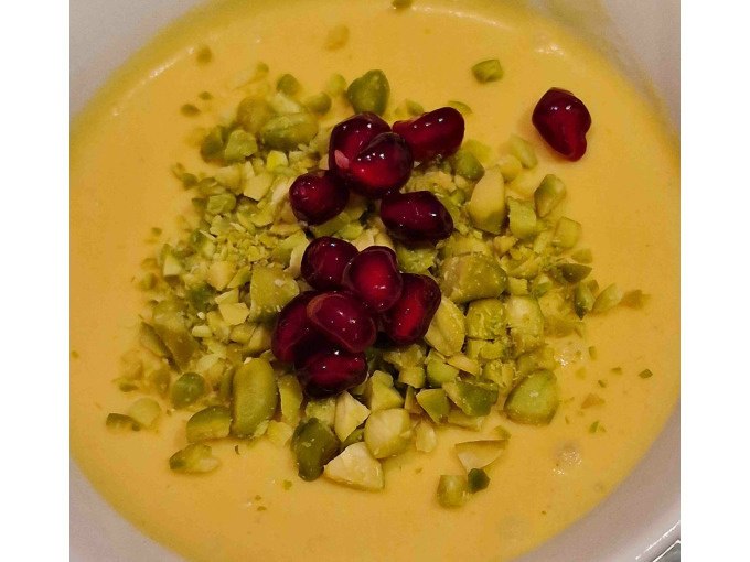 Ein cremiges gelbes Dessert, garniert mit gehackten Pistazien und Granatapfelkernen, präsentiert sich in einer Schale., © Kultweine-Kochwelten-Kunstücke - Kochschule Sonja Lenz Ein cremiges gelbes Dessert, garniert mit gehackten Pistazien und Granatapfelkernen, präsentiert sich in einer Schale., © Kultweine-Kochwelten-Kunstücke - Kochschule Sonja Lenz