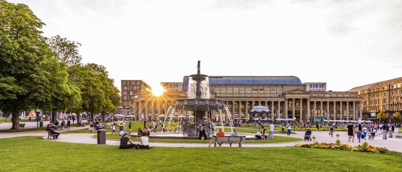 Schlossplatz in Stuttgart bei Sonnenuntergang, Menschen entspannen sich auf der Wiese, im Hintergrund der Königsbau und ein Brunnen., © Stuttgart-Marketing GmbH, Werner Dieterich