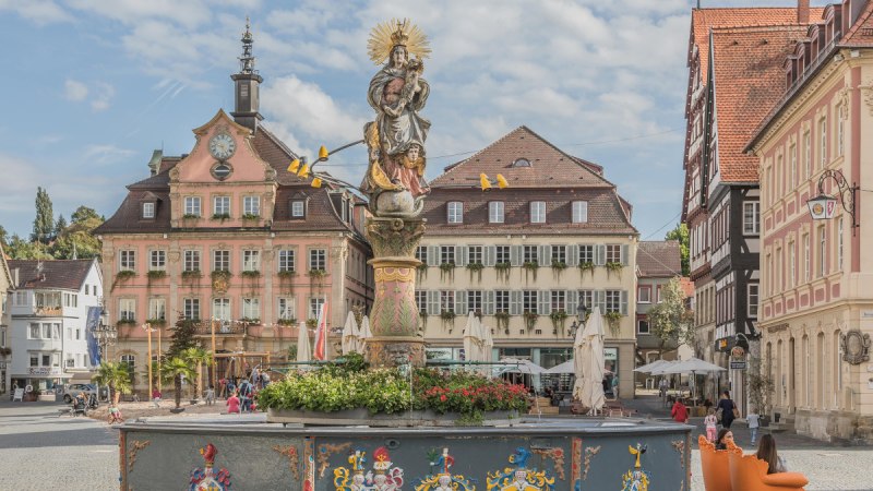 Historischer Marktplatz mit einem verzierten Brunnen und einem alten Rathaus im Hintergrund. Menschen flanieren und genießen die Atmosphäre. Historischer Marktplatz mit einem verzierten Brunnen und einem alten Rathaus im Hintergrund. Menschen flanieren und genießen die Atmosphäre.