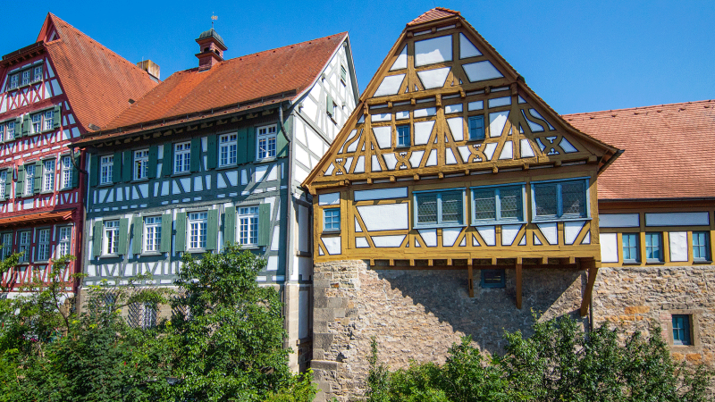 Fachwerkhäuser mit roten Dächern und grünen Fensterläden, umgeben von Bäumen, unter klarem blauem Himmel., © Stuttgart-Marketing GmbH, Achim Mende Fachwerkhäuser mit roten Dächern und grünen Fensterläden, umgeben von Bäumen, unter klarem blauem Himmel., © Stuttgart-Marketing GmbH, Achim Mende