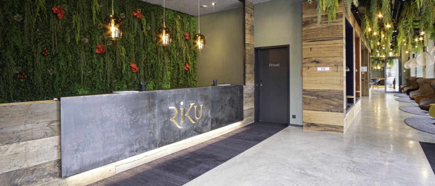 Moderne Hotelrezeption mit grüner Pflanzenwand, Holzverkleidung und stilvollen Leuchten. Der Empfangstresen trägt den Schriftzug 'RiKU'., © 13 6 Design GmbH (Judenhof 10, 89073 Ulm)