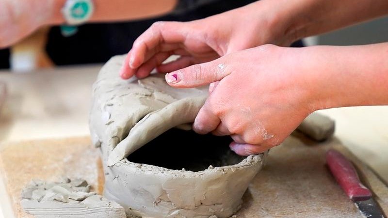 Zwei Personen formen Ton auf einem Tisch. Eine Person h&auml;lt ein St&uuml;ck Ton, w&auml;hrend die andere zuschaut. Ein Messer liegt daneben., &copy; Kunstschule Labyrinth