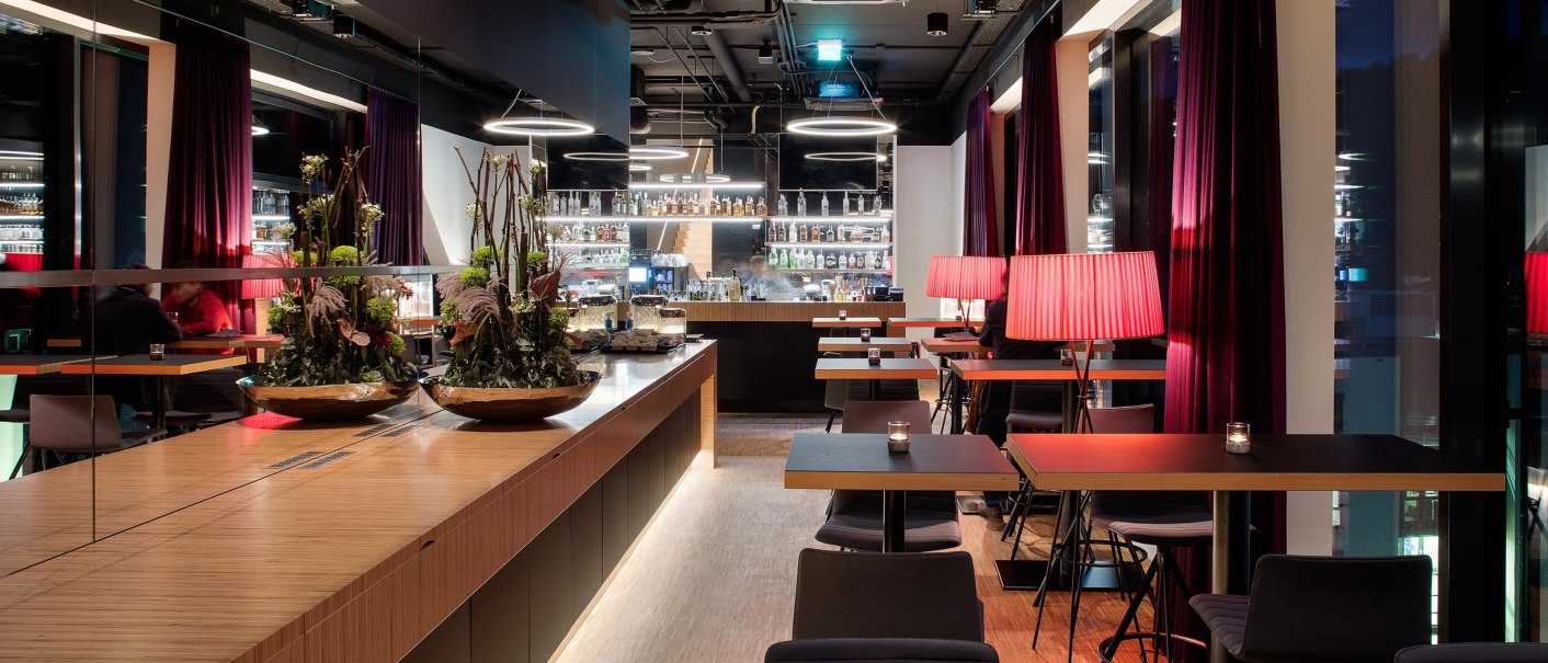 Moderne Bar im 7. Stock mit stilvoller Einrichtung, roten Lampen und Pflanzenarrangements. Gedämpfte Beleuchtung schafft eine gemütliche Atmosphäre., © Hotel am Remspark Moderne Bar im 7. Stock mit stilvoller Einrichtung, roten Lampen und Pflanzenarrangements. Gedämpfte Beleuchtung schafft eine gemütliche Atmosphäre., © Hotel am Remspark