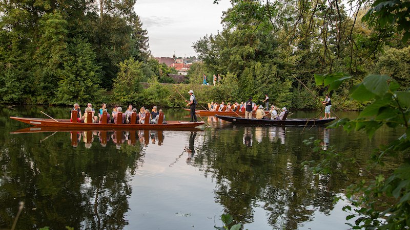 Zwei Boote mit Musikern fahren auf einem ruhigen Fluss, umgeben von &uuml;ppigem Gr&uuml;n. Die Szene wirkt friedlich und idyllisch., &copy; Stadtverwaltung Vaihingen an der Enz