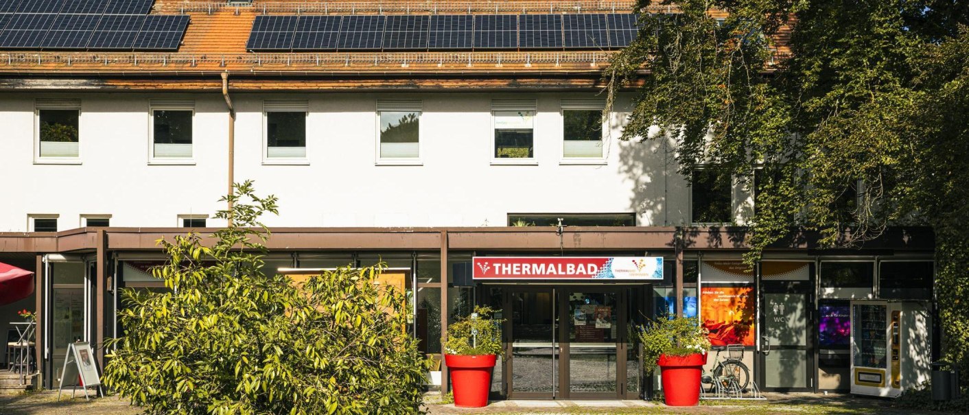 Eingang des Thermalbads in Bad Überkingen, umgeben von Pflanzen. Auf dem Dach sind Solarpanele installiert. Ein roter Blumentopf steht vor dem Eingang., © Stuttgart-Marketing GmbH, Sarah Schmid