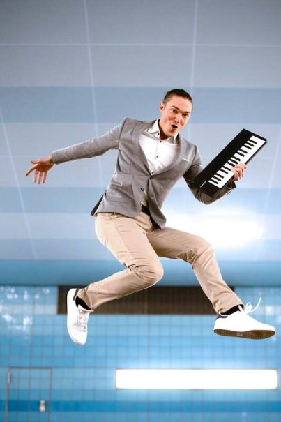 Mann in grauem Blazer springt mit Keyboard in der Hand vor blau gefliestem Hintergrund., © Stadtverwaltung Vaihingen an der Enz Mann in grauem Blazer springt mit Keyboard in der Hand vor blau gefliestem Hintergrund., © Stadtverwaltung Vaihingen an der Enz