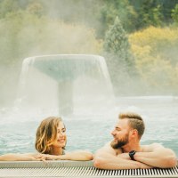 Zwei Personen entspannen in einem Außenpool der Paracelsus-Therme Bad Liebenzell. Im Hintergrund ein Wasserfall und bewaldete Hügel., © LOCHER Fotodesign & Manufaktur