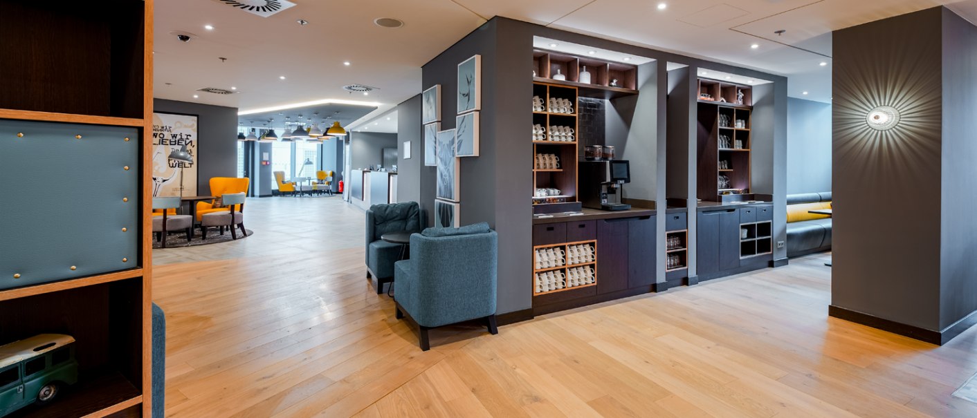 Moderner Frühstücksbereich mit Holzboden, blauen Sesseln, einer Kaffee-Ecke und gelben Stühlen im Hintergrund., © Premier Inn