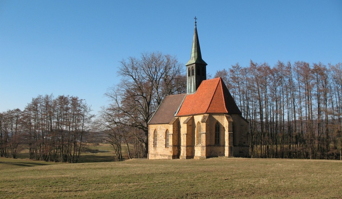 Die St.-Laurentius-Kapelle steht auf einer grünen Wiese, umgeben von kahlen Bäumen, unter einem klaren blauen Himmel., © Landkreis Göppingen