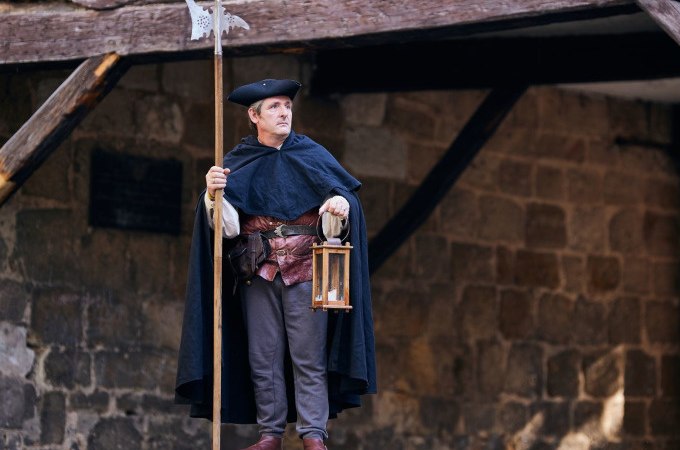 Ein Nachtwächter in historischer Kleidung steht mit Laterne und Hellebarde vor einer alten Steinmauer., © Esslinger Stadtmarketing &amp; Tourismus GmbH
