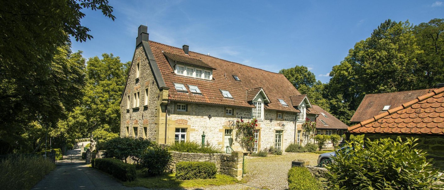 Ein charmantes, historisches Gebäude mit rotem Ziegeldach und blühenden Rosen an der Fassade, umgeben von üppigem Grün und einem gepflasterten Weg., © SMG, Sarah Schmid Ein charmantes, historisches Gebäude mit rotem Ziegeldach und blühenden Rosen an der Fassade, umgeben von üppigem Grün und einem gepflasterten Weg., © SMG, Sarah Schmid