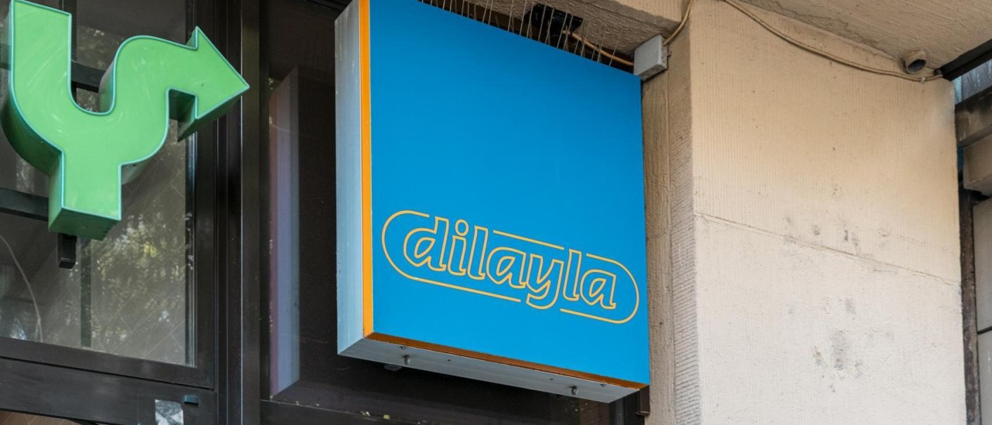 Blaues Schild mit gelber Aufschrift 'dilayla' an einer Gebäudewand, daneben ein grüner Pfeil., © Stuttgart Marketing GmbH, Sarah Schmid Blaues Schild mit gelber Aufschrift 'dilayla' an einer Gebäudewand, daneben ein grüner Pfeil., © Stuttgart Marketing GmbH, Sarah Schmid