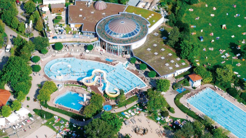 Luftaufnahme eines Freibads mit mehreren Schwimmbecken, Rutschen und einer großen Liegewiese. Menschen entspannen und schwimmen., © Wunndebad Winnenden Luftaufnahme eines Freibads mit mehreren Schwimmbecken, Rutschen und einer großen Liegewiese. Menschen entspannen und schwimmen., © Wunndebad Winnenden
