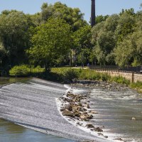 Fischtreppe in Nürtingen, umgeben von einem Fluss und üppiger Vegetation. Ein Schornstein ragt im Hintergrund auf., © SMG Mende Fischtreppe in Nürtingen, umgeben von einem Fluss und üppiger Vegetation. Ein Schornstein ragt im Hintergrund auf., © SMG Mende