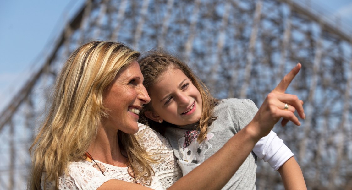 Eine Frau und ein M&auml;dchen l&auml;cheln und zeigen in die Ferne. Im Hintergrund ist eine unscharfe Struktur zu sehen., &copy; Erlebnispark Tripsdrill