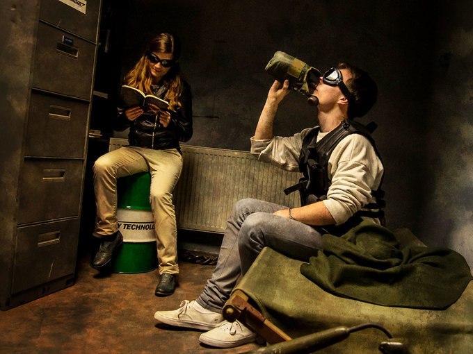 Zwei Personen in einem Raum, eine sitzt auf einem Fass und liest, die andere trinkt aus einer Flasche. Beide tragen Schutzbrillen., &copy; ExitGames Stuttgart