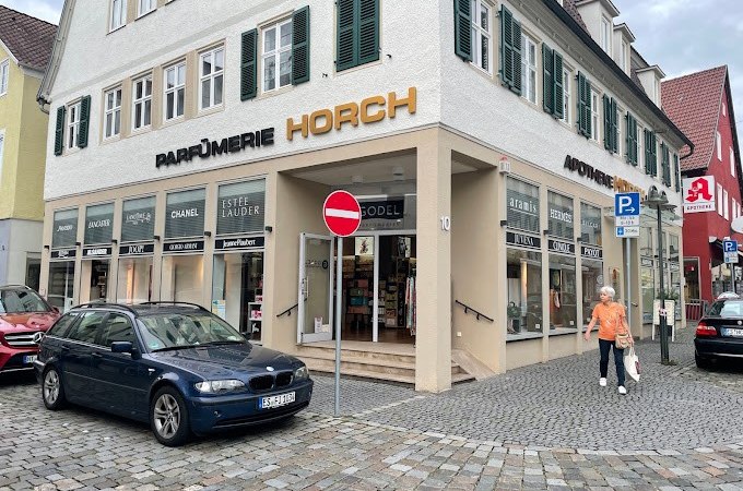 Parfümerie Godel in Nürtingen, Eckgebäude mit Schaufenstern, Autos parken davor, Passant geht vorbei., © Parfümerie Godel Parfümerie Godel in Nürtingen, Eckgebäude mit Schaufenstern, Autos parken davor, Passant geht vorbei., © Parfümerie Godel