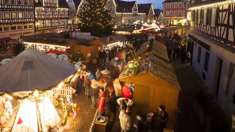 Ein festlich beleuchteter Weihnachtsmarkt mit Fachwerkhäusern, Ständen und einem großen Weihnachtsbaum. Menschen schlendern und genießen die Atmosphäre., © Stadt Schorndorf