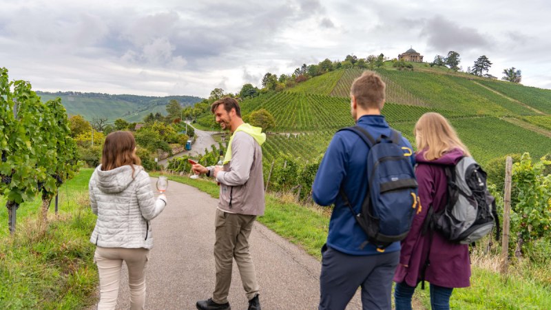 Menschen wandern auf einem Weinweg, halten Weingl&auml;ser. Im Hintergrund Weinberge und die Grabkapelle auf einem H&uuml;gel., &copy; Stuttgart-Marketing GmbH, Martina Denker