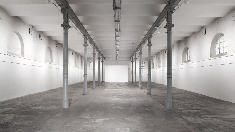 Eine leere, helle Halle mit hohen Decken und Säulen. Die Wände sind weiß gestrichen, und das Licht fällt durch Fensterbögen., © Kunstzentrum Karlskaserne Eine leere, helle Halle mit hohen Decken und Säulen. Die Wände sind weiß gestrichen, und das Licht fällt durch Fensterbögen., © Kunstzentrum Karlskaserne