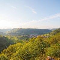 Panoramablick auf grüne Hügel und ein Tal mit einem Dorf. Die Sonne scheint von links, der Himmel ist klar mit wenigen Wolken., © SMG, Achim Mende