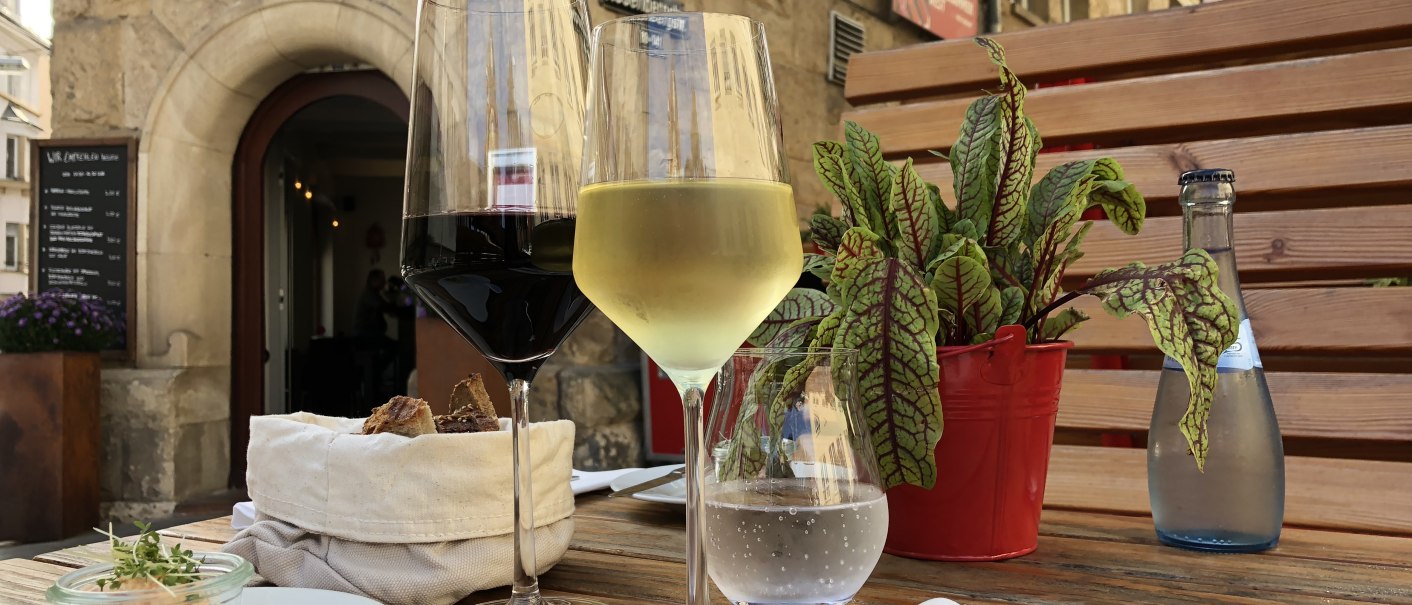 Ein Tisch mit Rot- und Weißweinglas, Brot, kleinem Gericht und Pflanze vor dem Restaurant 'Speisekammer West'., © Speisekammer West Ein Tisch mit Rot- und Weißweinglas, Brot, kleinem Gericht und Pflanze vor dem Restaurant 'Speisekammer West'., © Speisekammer West