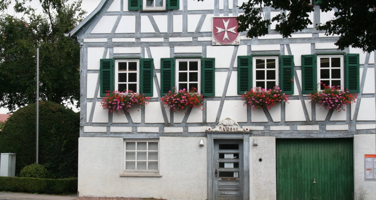 Fachwerkhaus mit grünen Fensterläden, blühenden Blumenkästen und einem Schild mit der Aufschrift 'Rathaus'. Ein Wappen ist über der Tür sichtbar., © Natur.Nah. Schönbuch & Heckengäu Fachwerkhaus mit grünen Fensterläden, blühenden Blumenkästen und einem Schild mit der Aufschrift 'Rathaus'. Ein Wappen ist über der Tür sichtbar., © Natur.Nah. Schönbuch & Heckengäu