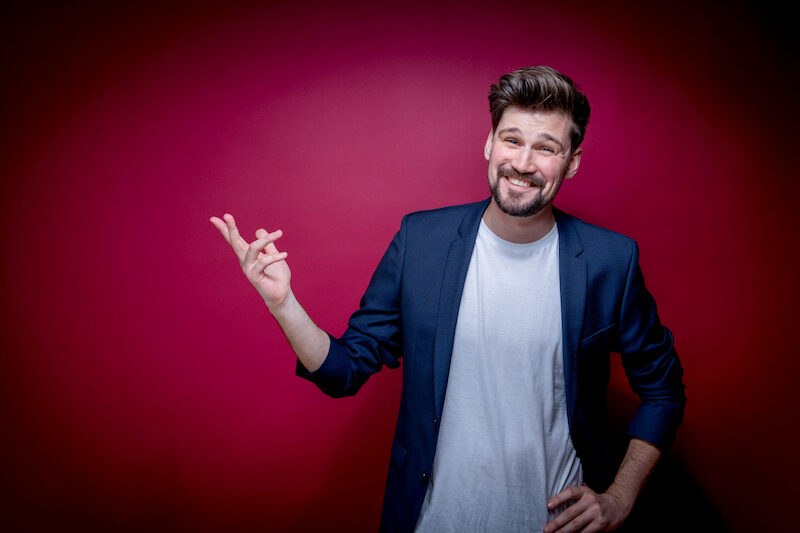 Mann in blauem Sakko und weißem T-Shirt lächelt vor rotem Hintergrund., © Stadt Leinfelden-Echterdingen, Kulturamt
