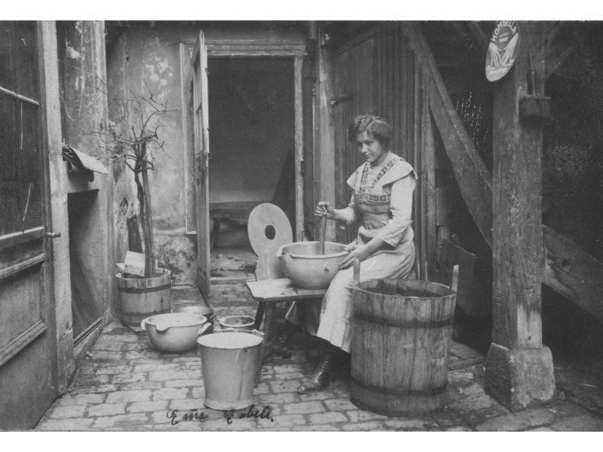 Eine Frau sitzt in einem Innenhof und w&auml;scht Kleidung in einer Sch&uuml;ssel. Um sie herum stehen Eimer und ein Waschbrett. Die Szene wirkt historisch., &copy; Stadt N&uuml;rtingen