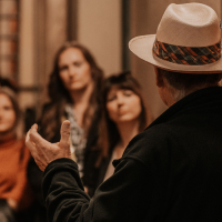 Ein Mann mit Hut erklärt einer Gruppe von Menschen etwas in einem Weinkeller. Die Zuhörer wirken interessiert., © Fellbacher Weingärtner eG Ein Mann mit Hut erklärt einer Gruppe von Menschen etwas in einem Weinkeller. Die Zuhörer wirken interessiert., © Fellbacher Weingärtner eG