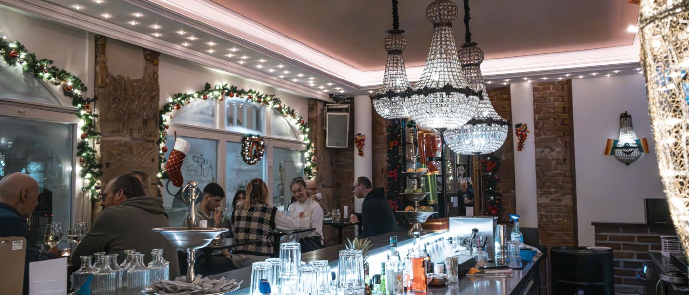 Festlich dekorierte Bar mit Kronleuchtern, Gästen an der Theke und weihnachtlichem Schmuck. Gläser und Flaschen stehen auf der Theke., © SMG Stuttgart Marketing GmbH - Sarah Schmid