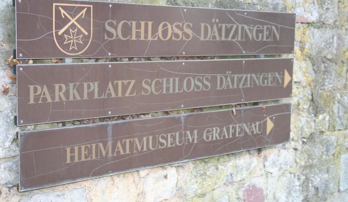 Wegweiser aus Holz zeigt Richtung Schloss Dätzingen und Heimatmuseum Grafenau. Schild mit Wappen an einer Steinmauer befestigt., © Natur.Nah. Schönbuch & Heckengäu