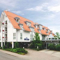 Modernes Hotel mit roten Ziegeldächern und weißen Wänden, umgeben von Bäumen und Pflanzen, an einer Straße gelegen., © Hotel Alber KG