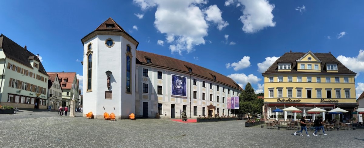 Historisches Geb&auml;ude in Schw&auml;bisch Gm&uuml;nd mit wei&szlig;er Fassade, angrenzendem Platz und Caf&eacute;s. Menschen spazieren bei sonnigem Wetter., &copy; T&M GmbH Schw&auml;bisch Gm&uuml;nd