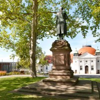 Statue auf der Schillerhöhe in Marbach am Neckar, umgeben von Bäumen. Im Hintergrund ein historisches Gebäude mit rotem Dach., © Corinna Jacobs