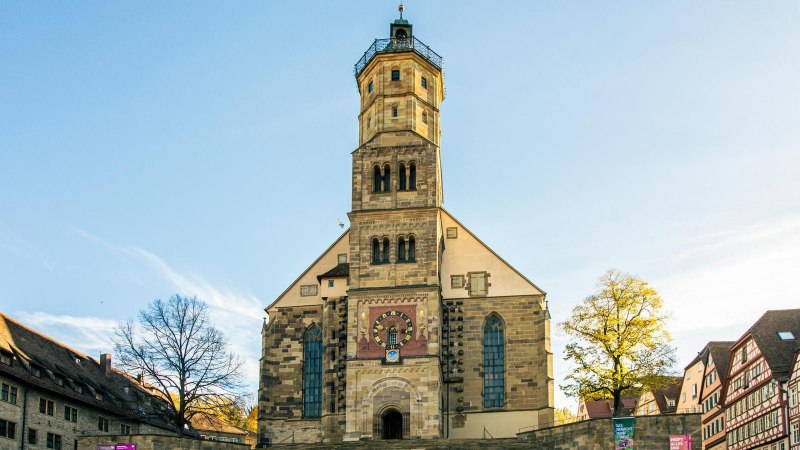 Die Kirche St. Michael in Schwäbisch Hall, umgeben von Fachwerkhäusern, erstrahlt im Sonnenlicht. Der Marktplatz ist menschenleer., © Stuttgart-Marketing GmbH, Sarah Schmid
