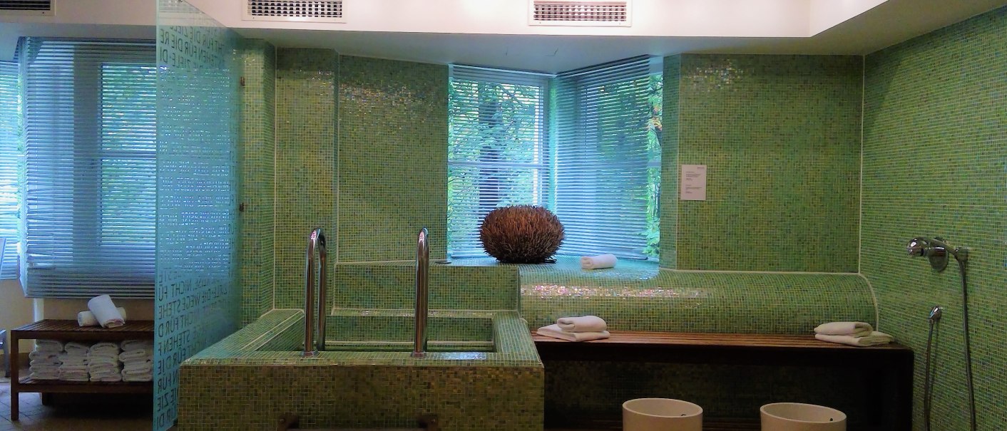 Moderner Raum mit Kneippbecken, grünen Mosaikfliesen, Handtüchern und zwei Fußbädern. Helle Beleuchtung und Fenster mit Jalousien., © relexa Waldhotel Schatten Moderner Raum mit Kneippbecken, grünen Mosaikfliesen, Handtüchern und zwei Fußbädern. Helle Beleuchtung und Fenster mit Jalousien., © relexa Waldhotel Schatten