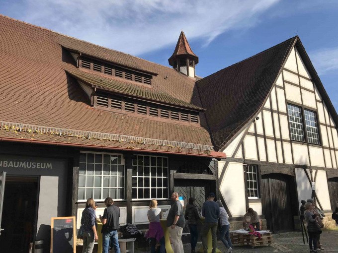 Menschen stehen vor einem Fachwerkgeb&auml;ude mit rotem Dach in Stuttgart-Uhlbach. Der Himmel ist blau und klar., &copy; Weingenuss Stuttgart