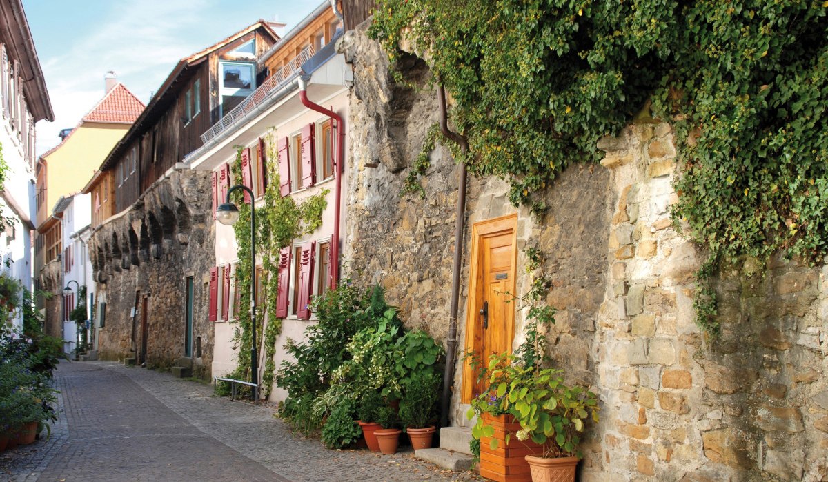 Enge Gasse in Reutlingen mit historischen Gebäuden, Stadtmauer und Pflanzen. Die Häuser haben rote Fensterläden und die Mauer ist mit Efeu bewachsen., © Mythos Schwäbische Alb im Landkreis Reutlingen e.V.